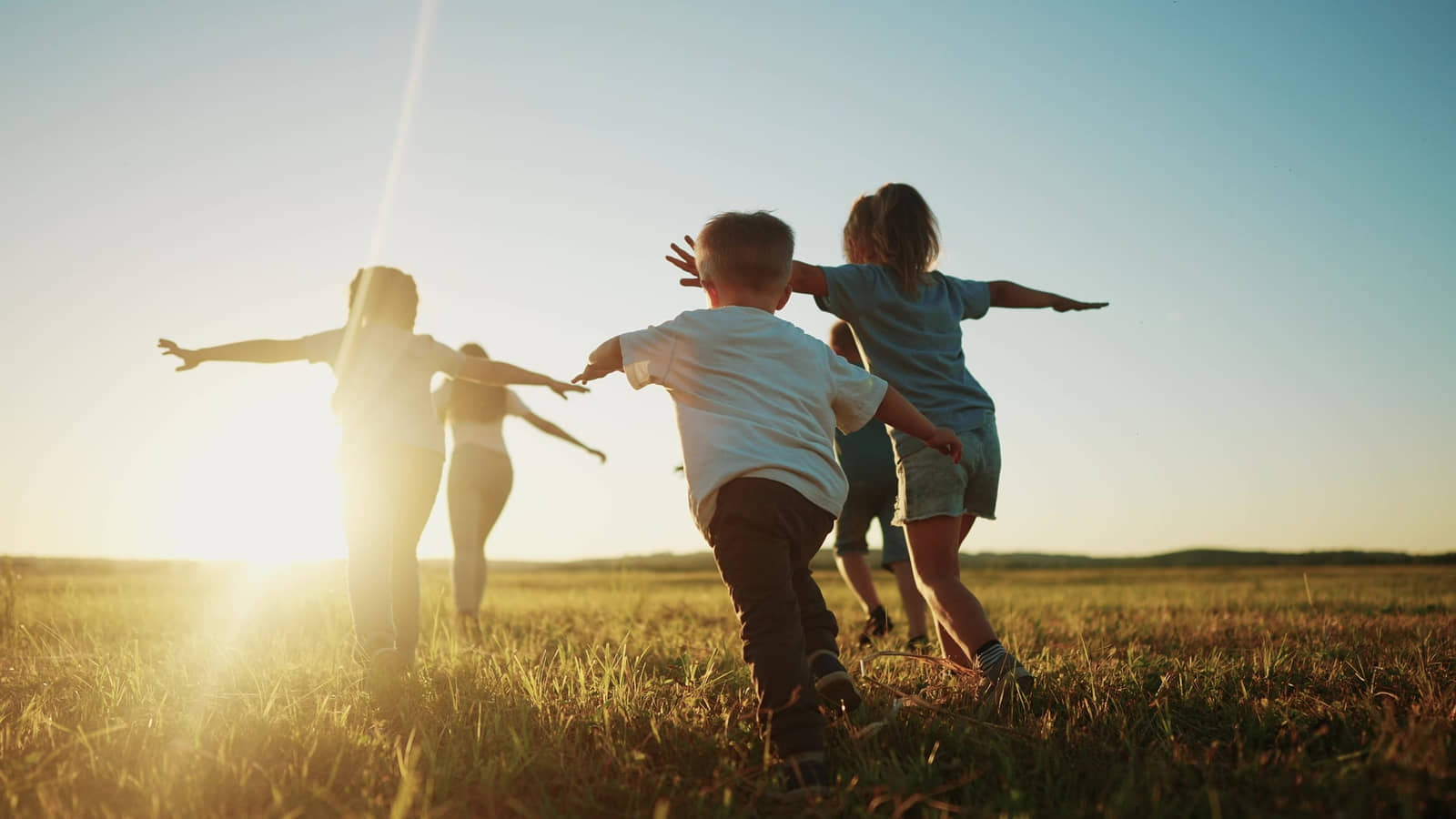 Children running across a sunny field with arms outstretched